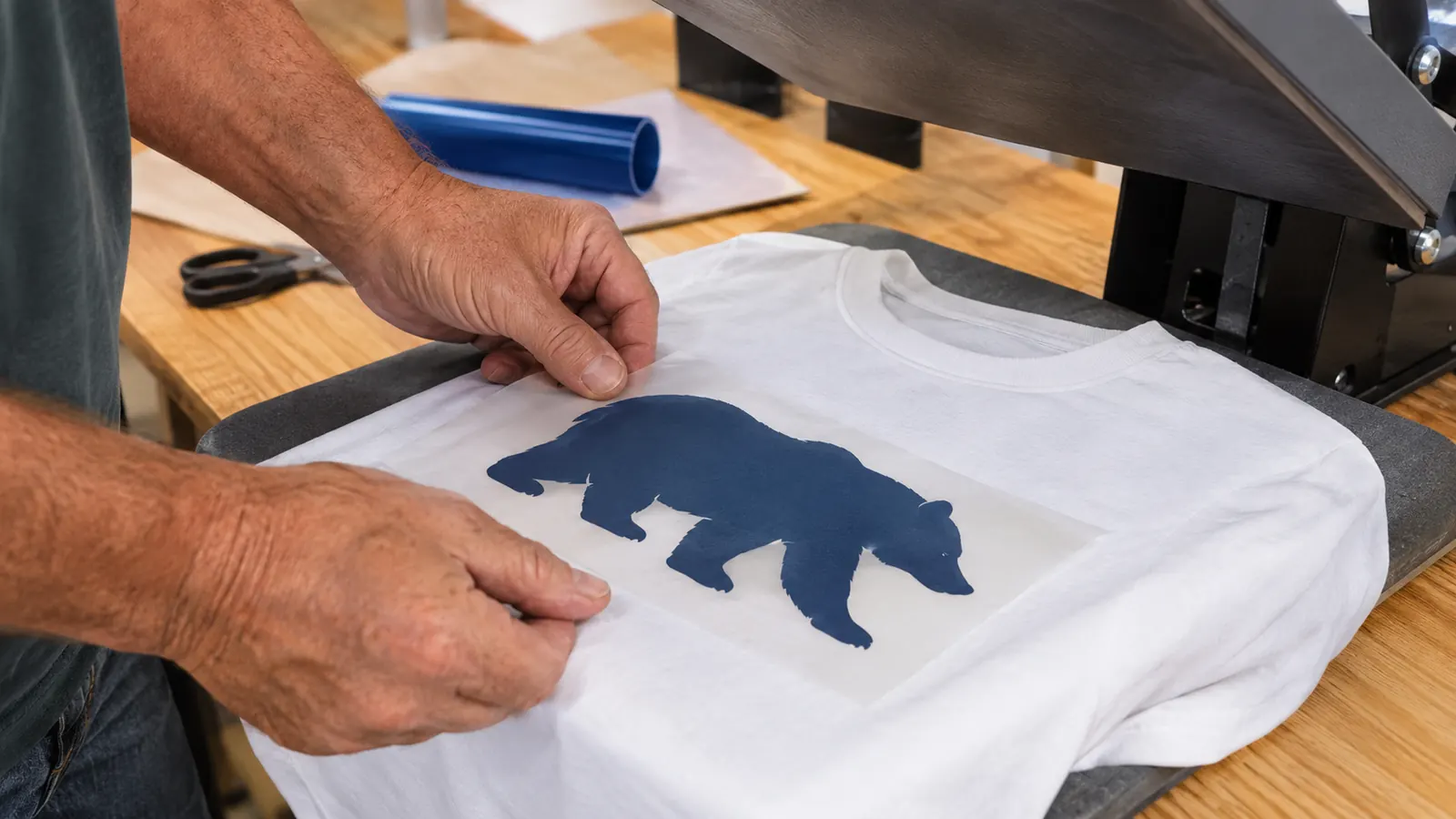 A hand placing a cut piece of iron-on vinyl onto a shirt on a heat press mat
